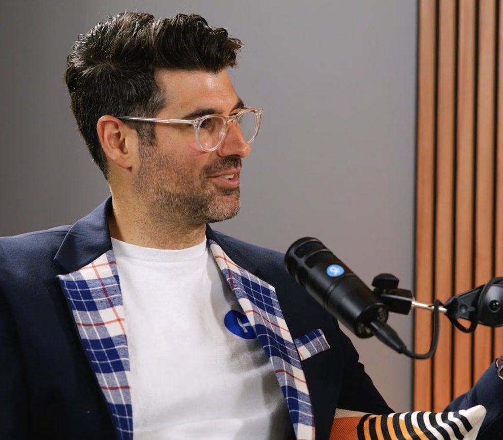 Podcast guest in a plaid blazer speaking into a studio microphone
